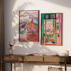 May include: Two framed abstract paintings with vibrant colors. The painting on the left depicts a colorful landscape with buildings and a body of water. The painting on the right shows a window with a view of a colorful landscape and boats.