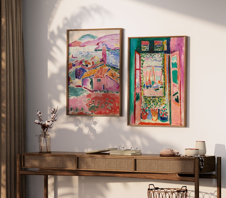 May include: Two framed abstract paintings with vibrant colors. The painting on the left depicts a colorful landscape with buildings and a body of water. The painting on the right shows a window with a view of a colorful landscape and boats.