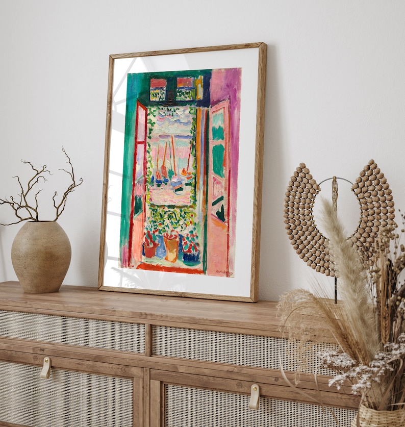 Puede incluir: Una pintura enmarcada de una escena abstracta colorida con una ventana que mira hacia un puerto con barcos. La ventana est&aacute; enmarcada por una pared rosa y verde. Hay plantas en macetas frente a la ventana.