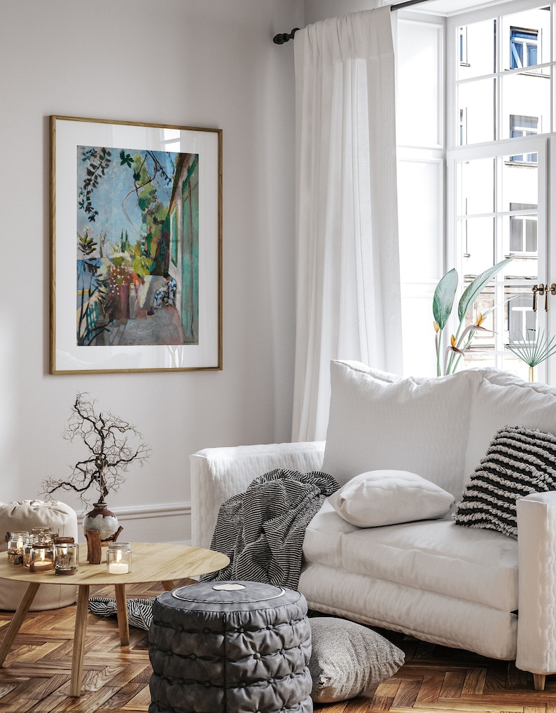 May include: A white sofa with a black and white striped throw blanket, a white pillow, and a black and white striped pillow. The sofa is in a living room with a wooden floor, a coffee table, and a framed painting of a garden scene.