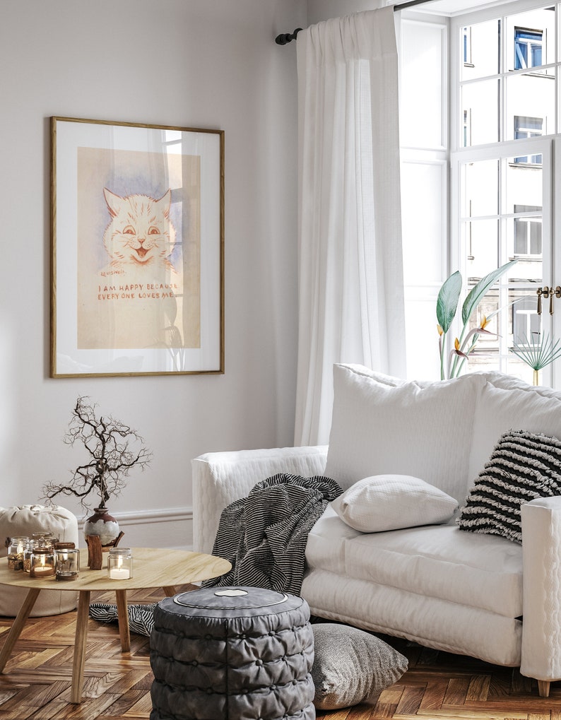 May include: A white framed print of a cartoon cat with the text "I am happy because everyone loves me". The print is hanging on a white wall in a living room with a white sofa, a throw blanket, and a coffee table with candles.