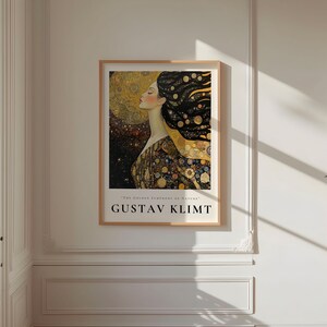 May include: A poster featuring a painting by Gustav Klimt. The painting depicts a woman with long flowing hair and a golden dress. The background is a mix of gold, black, and white.