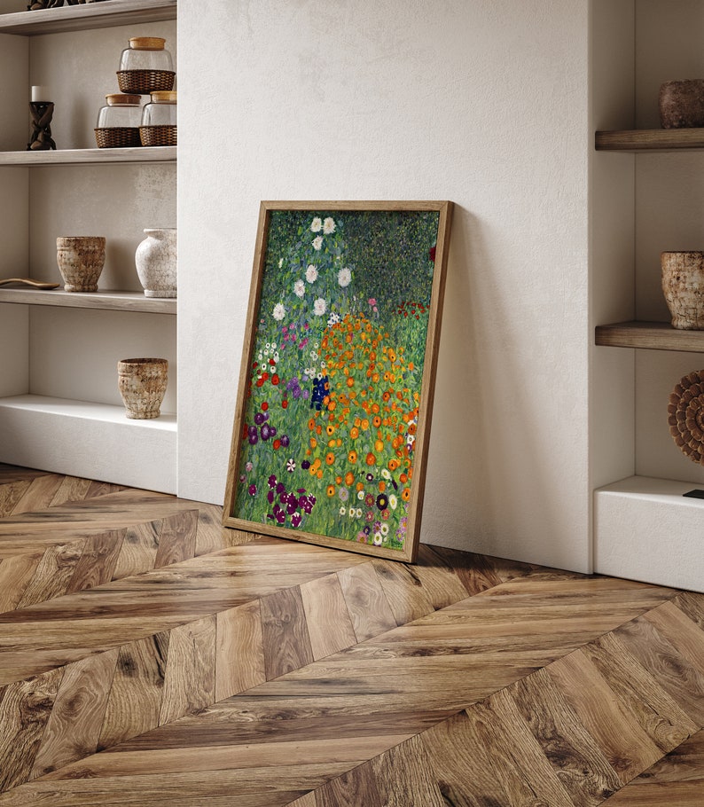 May include: A framed print of a painting depicting a field of colorful flowers. The flowers are mostly orange, yellow, and white, with some purple and blue accents. The background is a green field with a dark green forest in the distance.