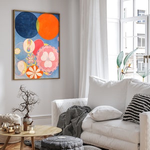 May include: An abstract art print in a gold frame features a composition of colorful circles and floral shapes. The artwork includes a large blue circle, an orange circle, and various smaller circles in pink, yellow, and red. The print hangs above a white sofa in a bright living room.