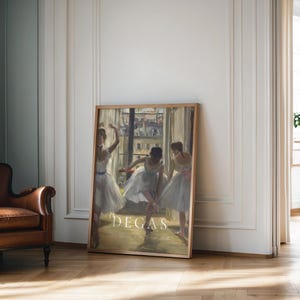 May include: A framed print of a painting by Edgar Degas depicting three ballerinas in a dance studio. The ballerinas are wearing white tutus and are in various poses. The painting is set against a backdrop of a window with a view of a city street.