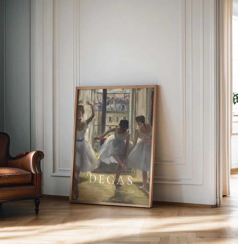 May include: A framed print of a painting by Edgar Degas depicting three ballerinas in a dance studio. The ballerinas are wearing white tutus and are in various poses. The painting is set against a backdrop of a window with a view of a city street.