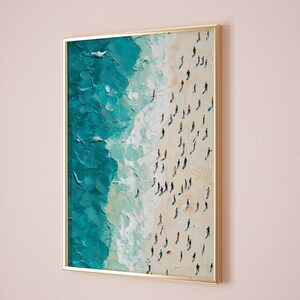 May include: A framed painting depicting a beach scene with turquoise water and white sand. The painting shows a large group of people walking along the beach, viewed from above.