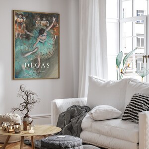 May include: A framed print of a painting by Edgar Degas depicting dancers in a ballet studio. The dancers are wearing light blue and green tutus and are in various poses. The painting is set against a light blue background. The print is framed in a gold frame and has the artist's name, "Degas", printed below the image.