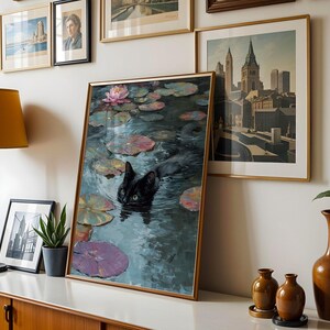 May include: A framed art print depicts a black cat swimming in a pond with lily pads and a pink water lily. The artwork is displayed on a white surface with other framed art, a lamp, and decorative vases.