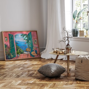 May include: A framed painting of a pink and green room with an open window overlooking a blue ocean. The painting is hanging on a white wall with a wooden floor. There is a small table with candles and a gray pillow on the floor.