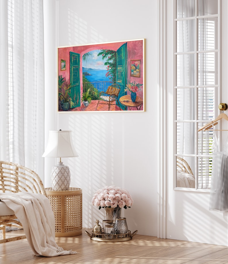 May include: A painting of a pink building with an open window overlooking a blue ocean. The window has green shutters and a wicker chair is sitting on the balcony. The painting is framed in gold.