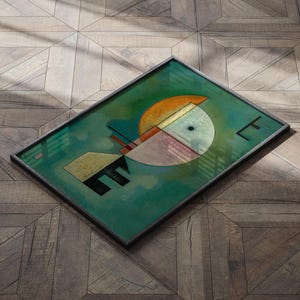 Może przedstawiać: Abstrakcyjny wydruk artystyczny w czarnej ramie. Grafika przedstawia geometryczne kształty w odcieniach zieleni, pomarańczy, beżu i czerni na tle turkusowego tła. Wydruk jest prostokątny i spoczywa na drewnianej powierzchni.