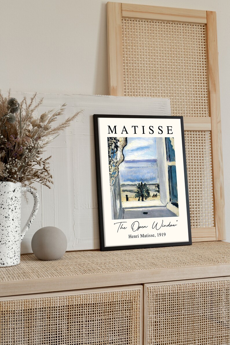 May include: A black framed print of a painting by Henri Matisse titled "The Open Window". The painting depicts a view from a window with a blue sky, sea, and palm tree.