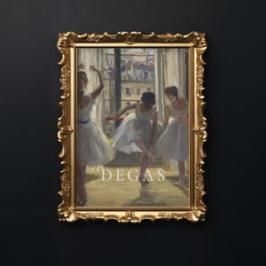 May include: A framed print of a painting by Edgar Degas depicting three ballerinas in a dance studio. The painting is in a gold frame with ornate details. The title of the painting is "Degas: The Dancers in a Rehearsal Hall" and is printed below the image.