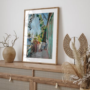 May include: A framed painting of a colorful landscape with a building and a person in the distance. The painting is in a wooden frame and is hanging on a wall.