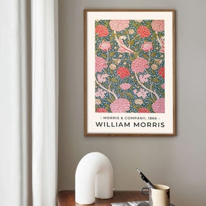 K&ouml;nnte beinhalten: Ein gerahmter Druck eines Blumenmusters in Rosa-, Gr&uuml;n- und Wei&szlig;t&ouml;nen. Der Druck tr&auml;gt den Titel "William Morris" und enth&auml;lt den Text "Morris & Company, 1866".