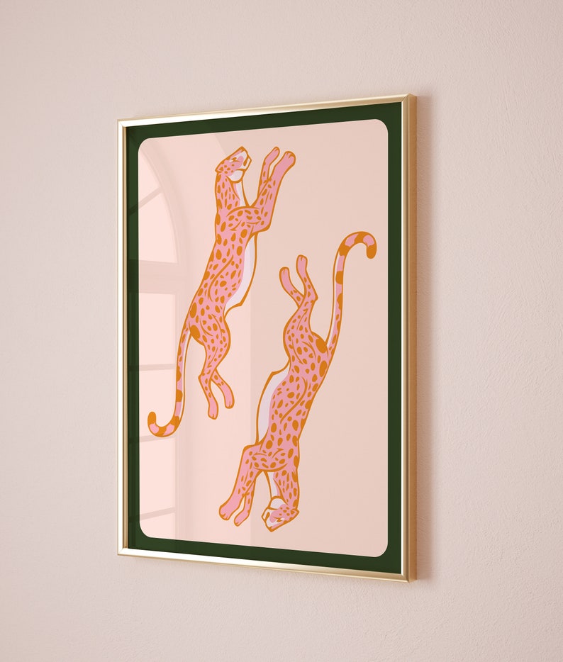 May include: A framed print featuring two pink and orange cheetahs with black spots, leaping in mid-air against a light pink background.