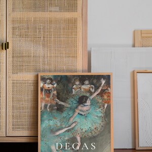 May include: A framed print of a painting by Edgar Degas depicting a group of dancers in a ballet studio. The dancers are wearing colorful tutus and are in various poses. The painting is titled "Dancing Dancers" and is signed "Degas".