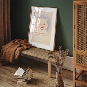 May include: A framed print of a white cat with a smiling face. The print has the text "I am happy because everyone loves me." The print is hanging on a green wall above a woven bench with a brown blanket draped over it. A wicker vase with dried flowers sits on the floor next to the bench.