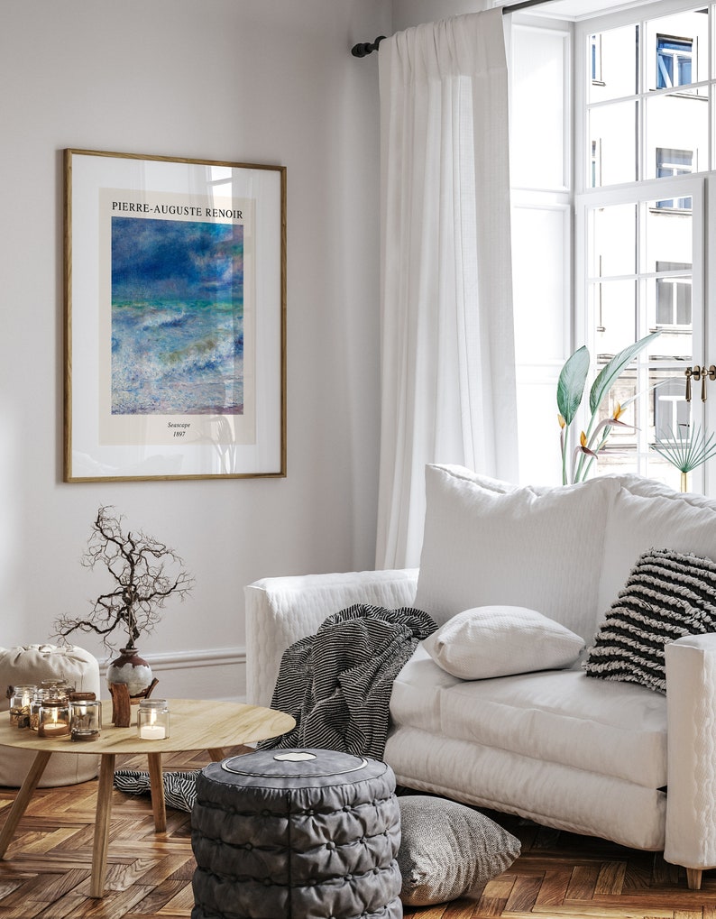May include: A framed print of a painting by Pierre-Auguste Renoir titled "Seascape 1887". The painting depicts a seascape with blue and white waves crashing against the shore. The print is hanging on a white wall in a living room setting.