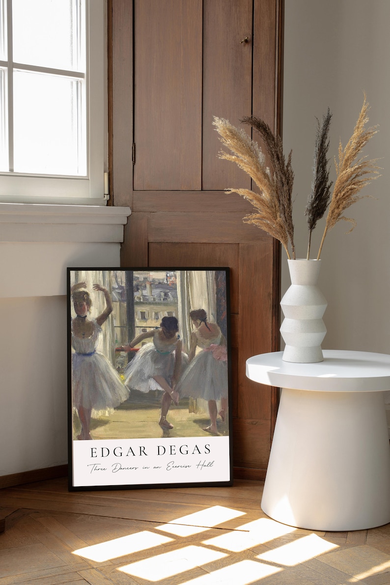 May include: A framed print of a painting by Edgar Degas titled "Three Dancers in an Exercise Hall". The painting depicts three ballerinas in white tutus practicing in a dance studio. The print is framed in black and has a white mat.