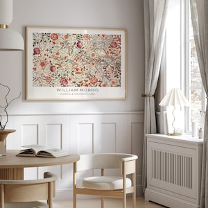 May include: A framed print of a floral pattern with the text "WILLIAM MORRIS - MORRIS & COMPANY, 1862" at the bottom. The print is hanging on a white wall in a room with a wooden table and chairs.
