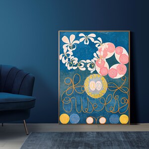 May include: A framed abstract painting with a blue background, featuring pink and white flowers, gold swirls, and yellow circles. The painting is hanging on a blue wall.