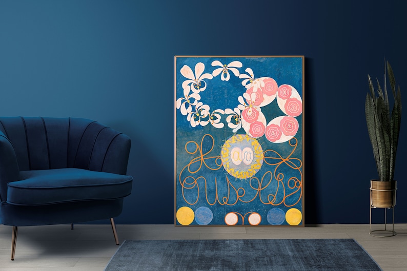 May include: A framed abstract painting with a blue background, featuring pink and white flowers, gold swirls, and yellow circles. The painting is hanging on a blue wall.