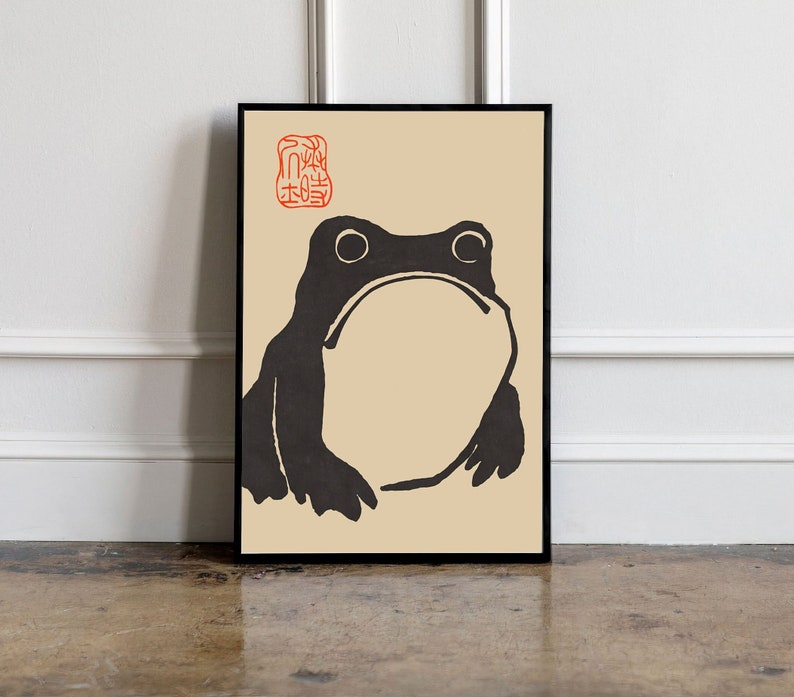 May include: A black and white illustration of a frog on a beige background. The frog is facing forward with its mouth closed. The image is framed in a black frame.