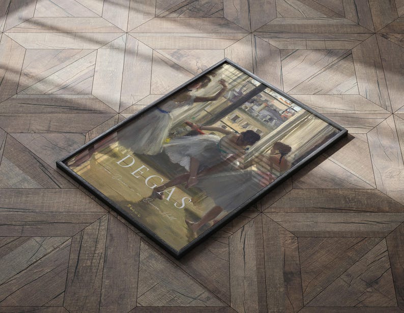 May include: A framed print of a painting by Edgar Degas depicting dancers in a ballet studio. The dancers are wearing white tutus and are in various poses. The painting is set against a background of a window with a view of a city street.