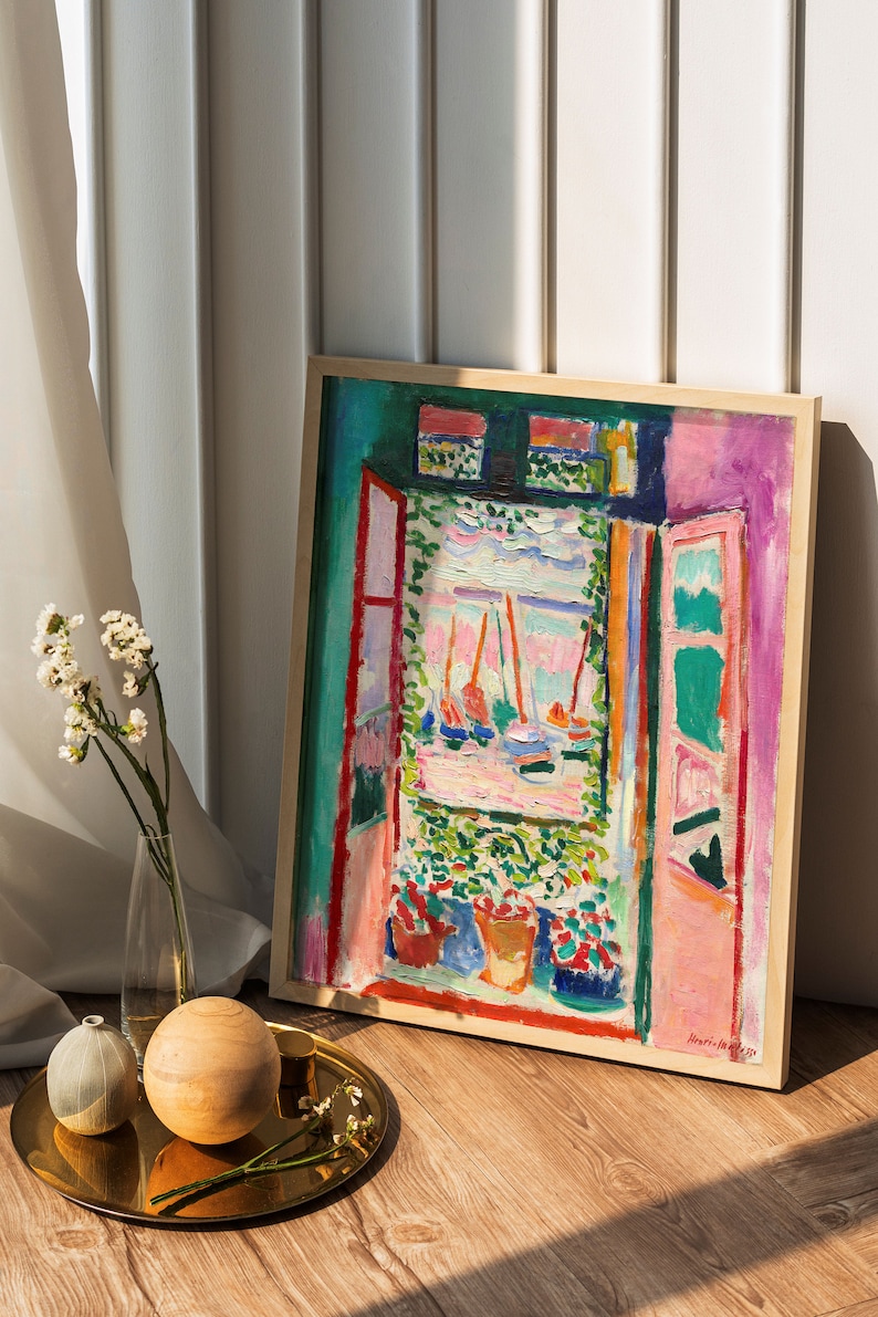 Puede incluir: Una pintura enmarcada de un paisaje colorido con una vista de ventana de barcos y un cielo rosa. La pintura est&aacute; en un marco de madera y est&aacute; sentada en un suelo de madera.