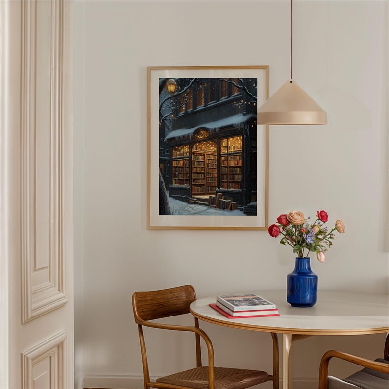 May include: A framed print of a bookstore with a snowy street scene at night. The bookstore is lit up with warm yellow lights and has a sign that reads "The Book Nook".