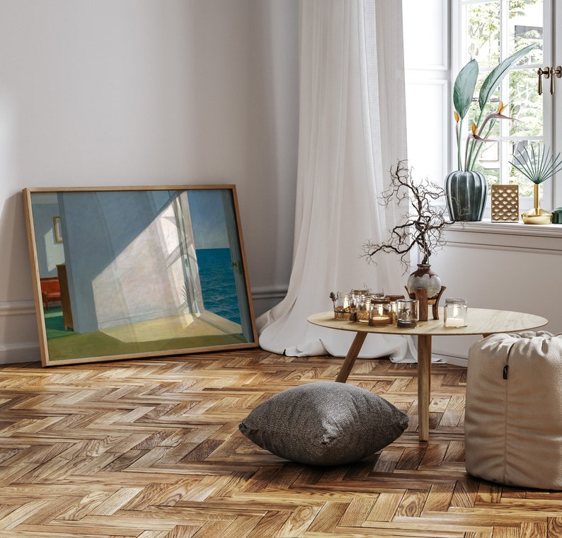 May include: A framed print of a painting depicting a room with a window overlooking the sea. The room is bathed in sunlight, and the window is open. The print is hanging on a white wall, and there is a wooden floor in the foreground.