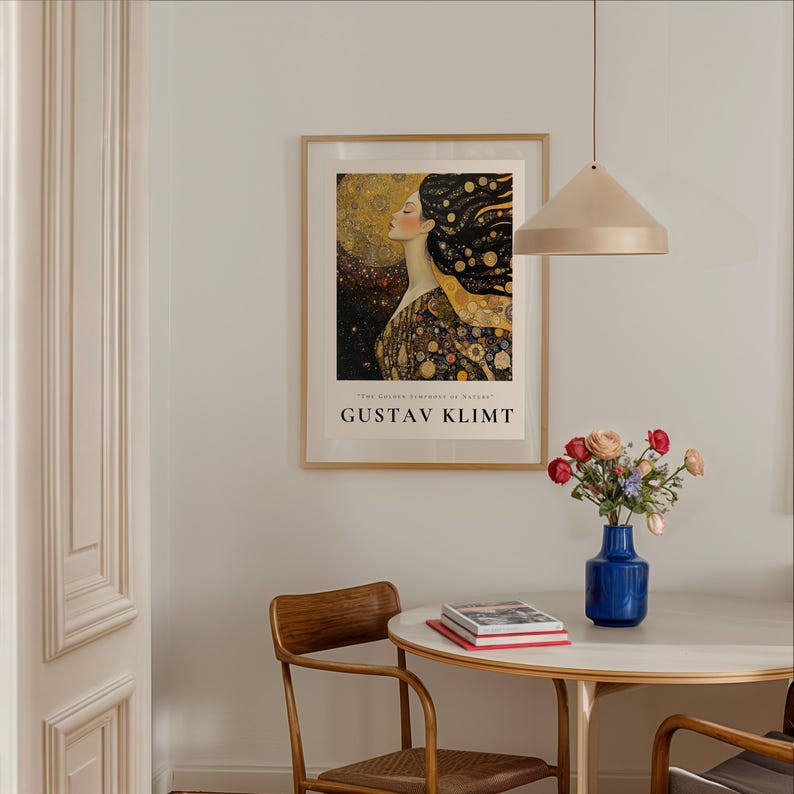 May include: A framed poster of a painting by Gustav Klimt, featuring a woman with flowing hair and a golden background. The poster is hanging on a white wall above a round table with two chairs.