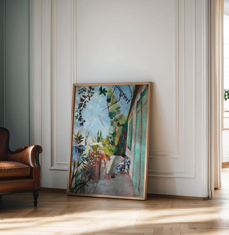 May include: A framed painting depicting a colorful outdoor scene with a person sitting on a patio. The painting features a green door, lush greenery, and a blue sky.