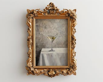 May include: A gold-framed painting of a martini glass with an olive on a white tablecloth.
