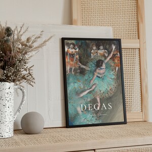 May include: A black framed poster with a painting of dancers in a green and blue color scheme. The poster has the text "Degas" in white lettering at the bottom.
