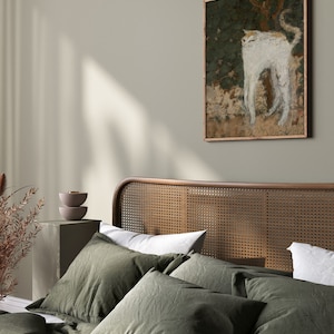 May include: A green linen bedding set with a woven headboard and a framed painting of a white cat in a forest setting.