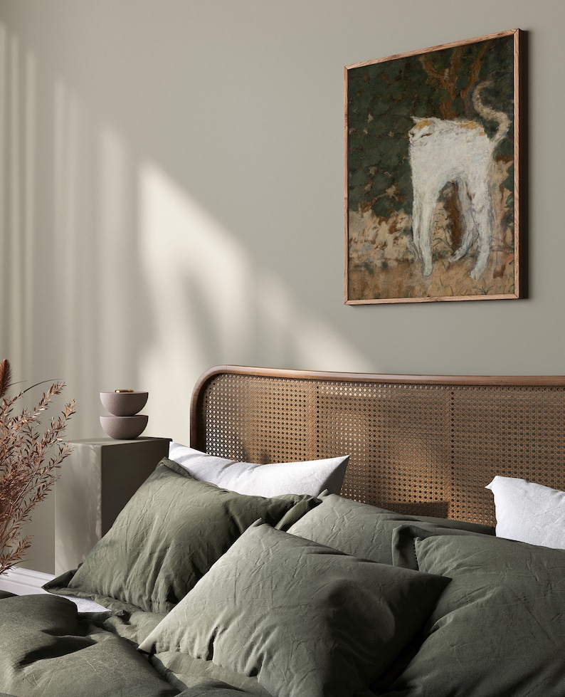 May include: A green linen bedding set with a woven headboard and a framed painting of a white cat in a forest setting.