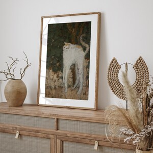 May include: A framed painting of a white cat with orange markings standing in a forest setting. The cat is looking to the left of the frame. The painting is in a wooden frame and is hanging on a wall.