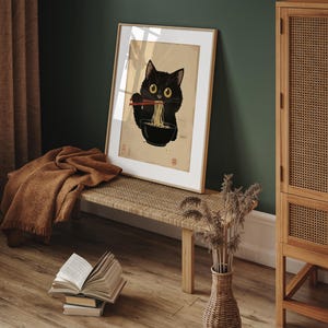 Puede incluir: Una impresi&oacute;n enmarcada de un gato negro comiendo fideos ramen con palillos. El gato mira al espectador con una expresi&oacute;n juguetona. La impresi&oacute;n est&aacute; sobre un fondo marr&oacute;n claro con un borde blanco.