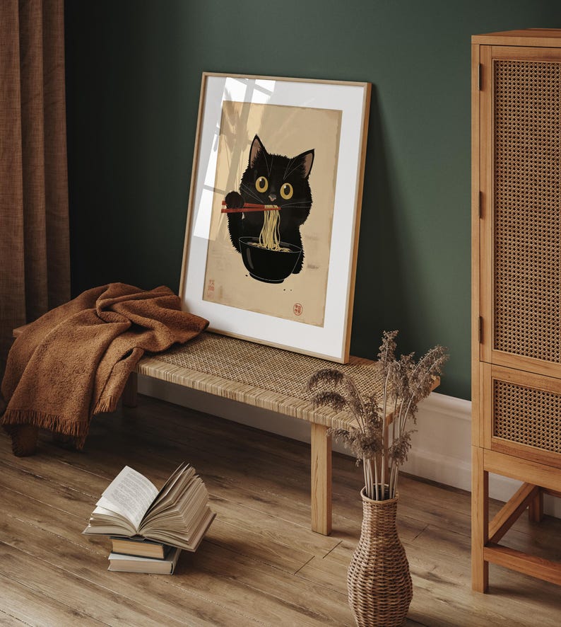 Puede incluir: Una impresi&oacute;n enmarcada de un gato negro comiendo fideos ramen con palillos. El gato mira al espectador con una expresi&oacute;n juguetona. La impresi&oacute;n est&aacute; sobre un fondo marr&oacute;n claro con un borde blanco.