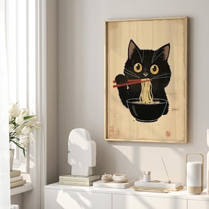 Puede incluir: Un gato negro con grandes ojos amarillos est&aacute; comiendo fideos de un taz&oacute;n con palillos. El gato est&aacute; sentado sobre un fondo de madera con texto japon&eacute;s.