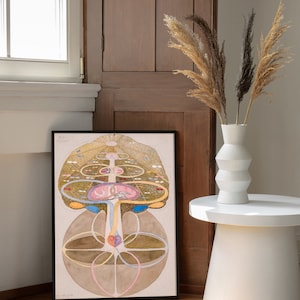 May include: A framed print of a detailed illustration of a tree of life with intricate branches, leaves, and roots. The tree is surrounded by circles and other geometric shapes, and the colors are mostly shades of brown, gold, and pink.