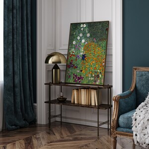 May include: A painting of a field of flowers in various shades of pink, yellow, white, and purple. The painting is framed and hanging on a wall above a shelf with books and a lamp.