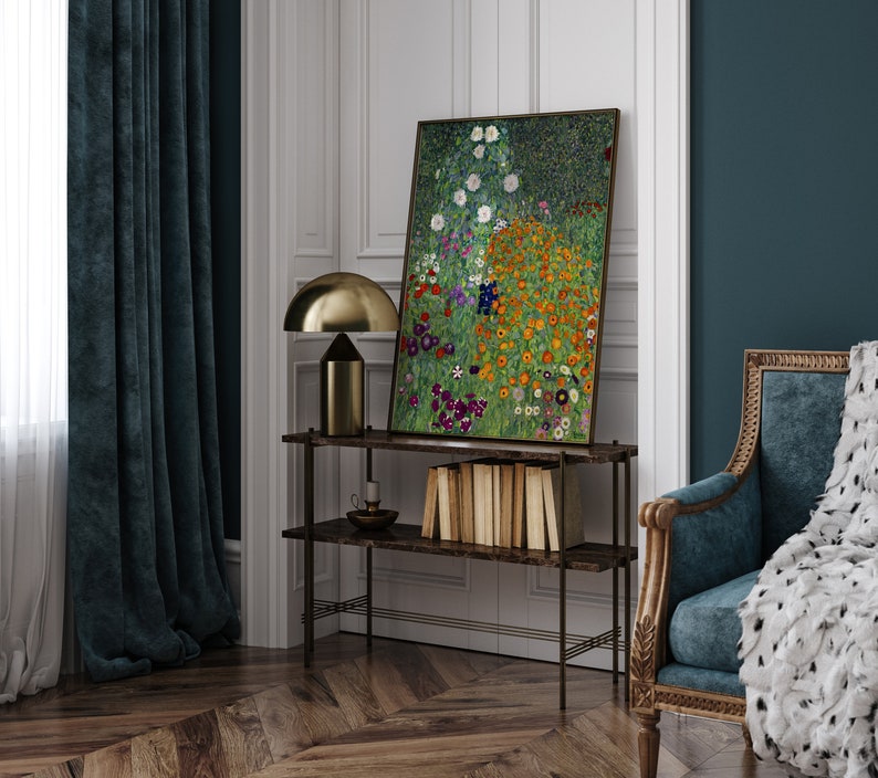 May include: A painting of a field of flowers in various shades of pink, yellow, white, and purple. The painting is framed and hanging on a wall above a shelf with books and a lamp.
