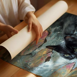May include: A rolled-up canvas print featuring a black cat with green eyes amidst water lilies. The artwork has a painterly style with soft blues, greens, pinks, and yellows. The canvas is being unrolled on a wooden surface.