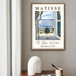 May include: A framed print of a painting by Henri Matisse titled "The Open Window". The painting depicts a window with a view of a palm tree and the sea. The text "Henri Matisse, 1919" is printed below the painting.