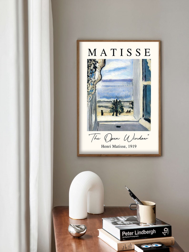 May include: A framed print of a painting by Henri Matisse titled "The Open Window". The painting depicts a window with a view of a palm tree and the sea. The text "Henri Matisse, 1919" is printed below the painting.