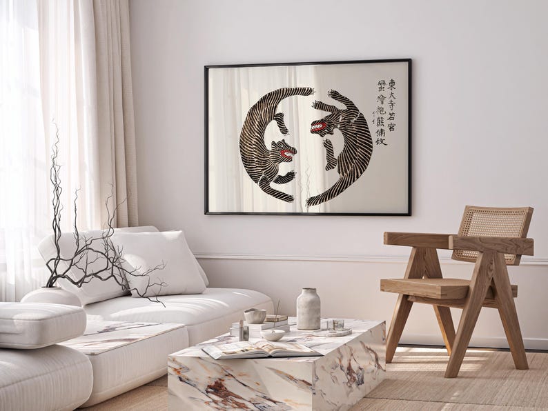 May include: A black framed print of two black and white stylized tigers facing each other in a circle. The print is hanging on a white wall above a white couch and a wooden chair. The print includes Chinese characters in black.